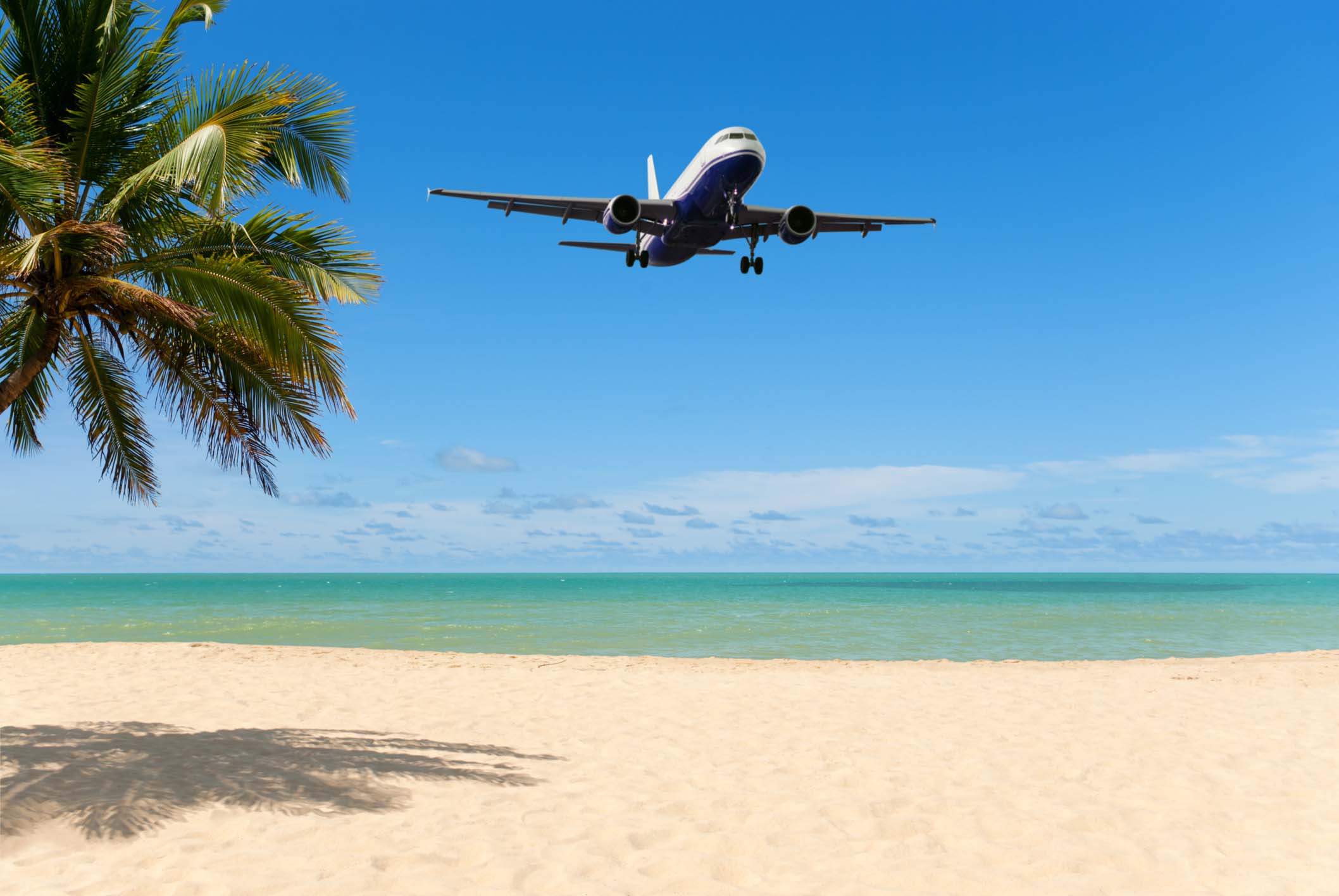 An airplane flying close over a tropical beach