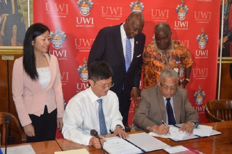 Minister of Health Dr. Fenton Ferguson (centre, standing), observes while Principal of the University of the West Indies, Professor Archibald McDonald (right), and Deputy General Manager at China Engineering Company (CHEC), Qiwu Yang (left), sign a M